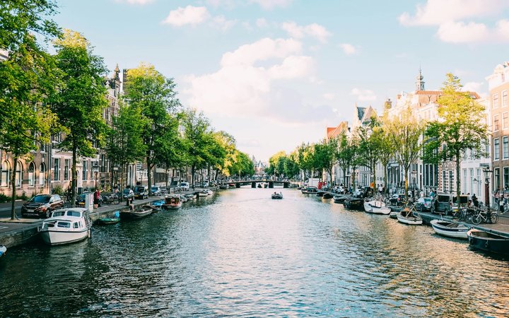 Boats on an Amsterdam canal lined with Dutch canal houses and green trees