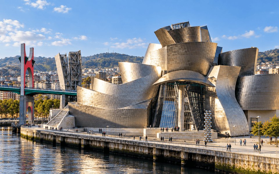 The metallic Guggenheim Museum Bilbao along the riverfront beside the red-arched La Salve Bridge under a clear blue sky