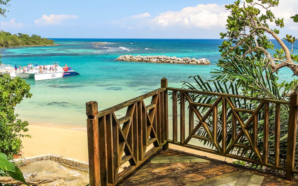 Turquoise bay and sandy beach seen from a wooden balcony with tropical leaves in Ocho Rios, Jamaica